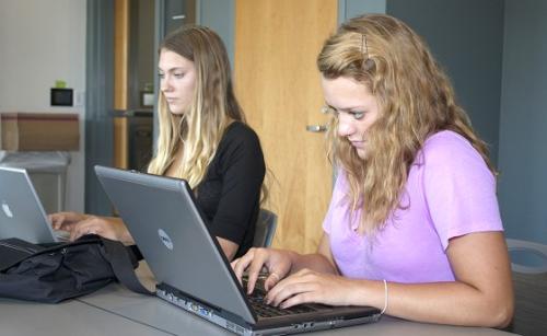 Two students type notes on their laptops