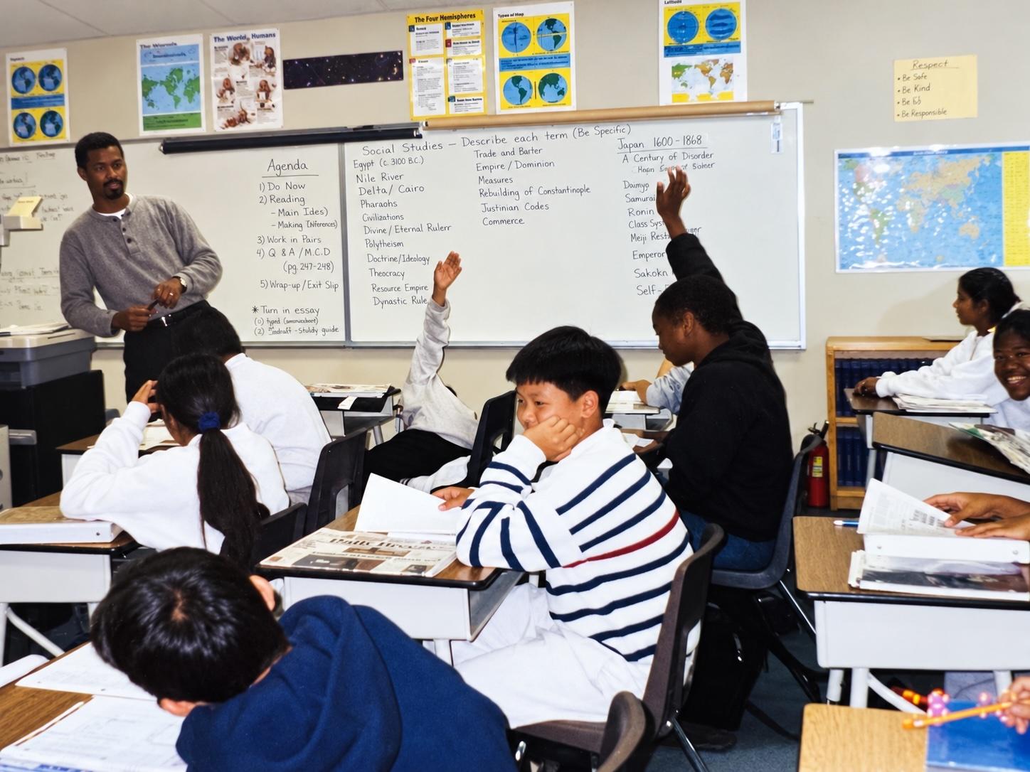 A young Darnell Horton stands at the front of a classroom beside a whiteboard of social studies terms, as seventh graders at their desks raise their hands.