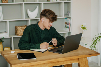 Young man attending online high school at his desk with laptop and notebook