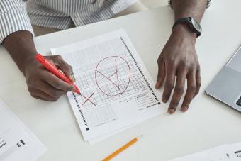 Hand marking corrections on a bubble answer sheet with a red pen
