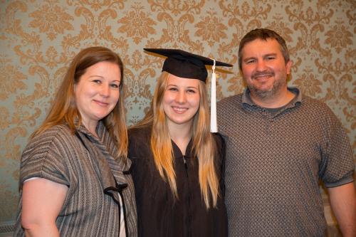 UT High School graduate in cap and gown smiles with her parents