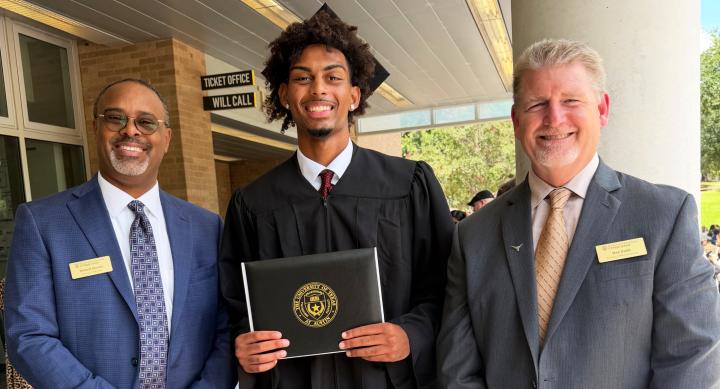 Ian Parham proudly displays his diploma wearing cap and gown, with Principal Darnell Horton and Dan Diehl